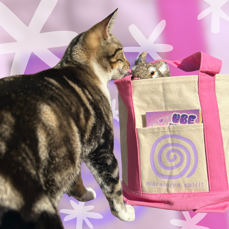 Image of a striped cat sniffing a rabbit in a tote bag. Text on the tote bag says Marahuyo Spirit.