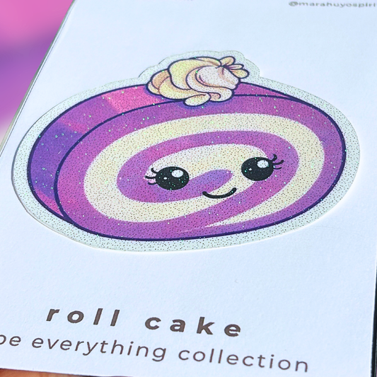 Close up image of a card with a ube roll cake design die cut decal held by a hand against a colorful background